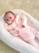 Newborn baby in pink knit outfit with pacifier lying on white DockATot Deluxe+ baby lounger