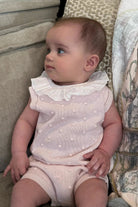 Baby girl in a pink knitted frill romper with white lace collar sitting on a beige couch