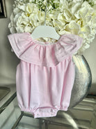 Pink baby girl summer romper with ruffled neckline hanging on white hanger, white flowers background