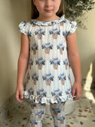 Child wearing matching blue hydrangea floral print top and leggings with striped background and ruffle details