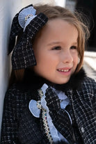 Smiling young girl wearing a black and white tweed bow and coat with fur collar detail