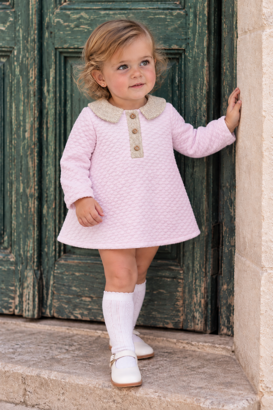 AW26 Lor Miral Baby Girls Pink Spanish Waffle Dress, featuring a textured waffle pattern, collar, and three buttons. Available in sizes 3 Months, 6 Months, 12 Months, 18 Months, and 24 Months.