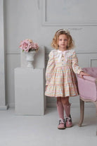 Little girl in vintage pastel floral dress with lace collar, pink knee socks, and matching shoes standing by pink chair