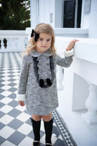 Young girl in black and white tweed dress with velvet bows standing on checkered patio