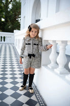 Young girl in black tweed shorts set with black knee-high socks and gold shoes on checkered floor