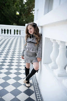 Young girl wearing black tweed shorts and ruffled top on a black-and-white tiled terrace