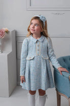 Young girl wearing blue checkered long sleeve dress with pearl buttons and matching headband in elegant room