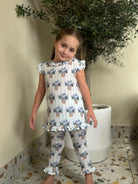 Little girl in matching blue hydrangea print loungewear set with ruffles, standing indoors by potted plant
