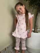 Young girl in pink striped loungewear set with bow patterns and ruffles standing indoors by large white planter