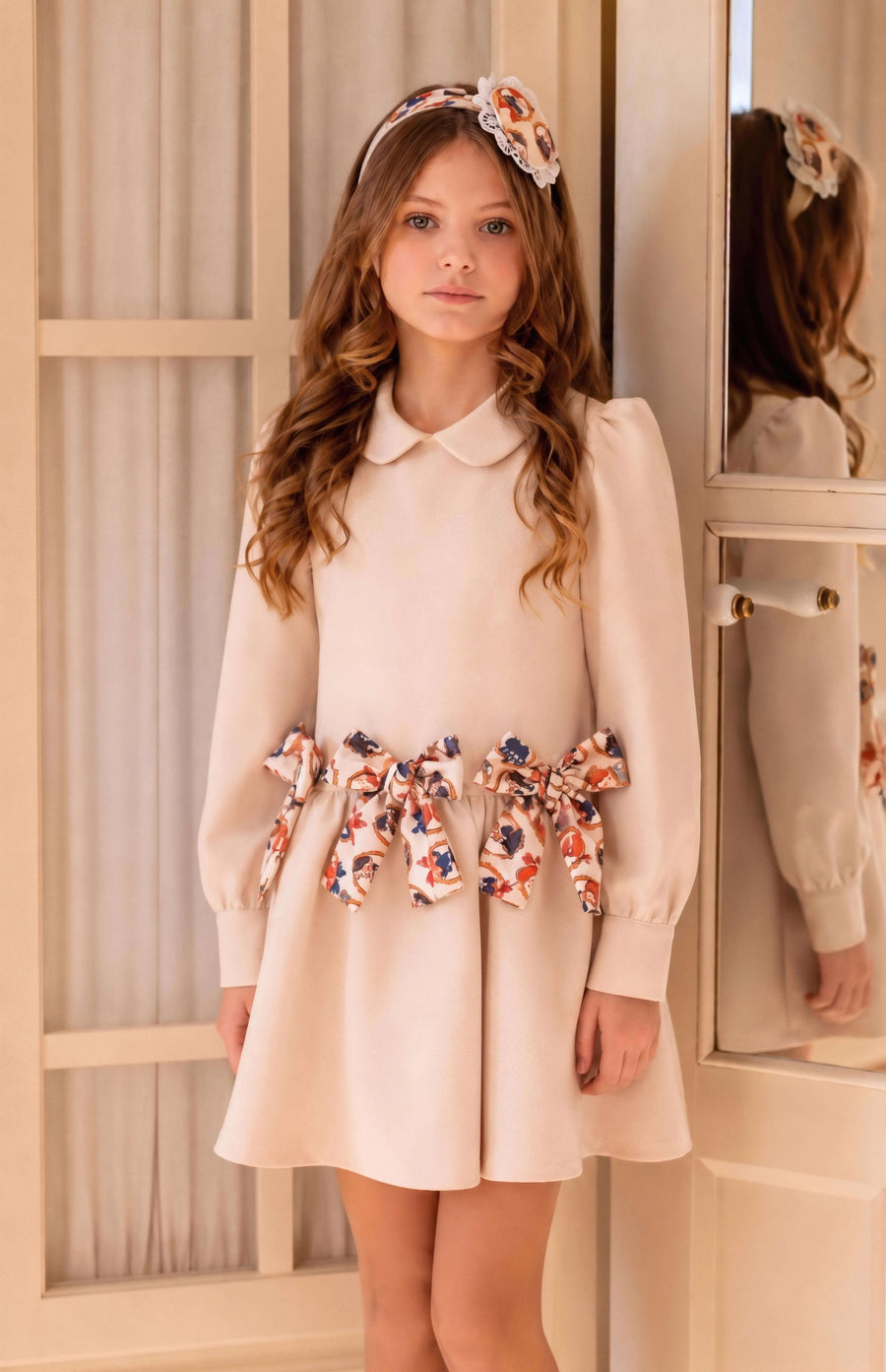 AW26 Rochy Girls Cream Teddy Bear Bow Detail Dress featuring teddy bear print bows, rounded collar, long sleeves, and flared skirt. Available in sizes 2 to 8 years.