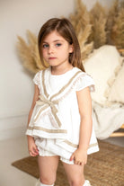Young girl wearing cream and camel sailor short set in a cozy indoor setting with pampas grass
