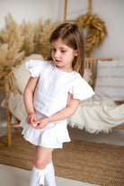 Young girl in ivory linen pleated short set with ruffled sleeves in cozy neutral room