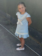 Young girl wearing a baby blue linen sailor A-line dress with beige trim standing outdoors