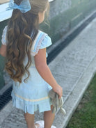 Young girl with long wavy hair wearing a baby blue linen sailor dress holding a stuffed toy outdoors