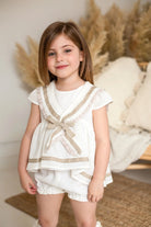 Young girl wearing cream and camel sailor short set with decorative bow in cozy neutral room