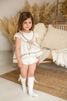 young girl wearing cream and camel sailor short set with knee-high socks in cozy neutral room