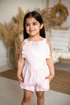 Smiling girl in a pink linen frilly jumpsuit standing indoors with pampas grass decor