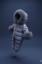 Blue shiny padded baby snowsuit with fur trim on hood and cuffs against a dark background