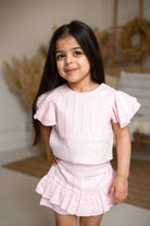 Smiling young girl in light pink ruffled dress posing indoors with blurred rustic decor background