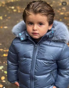 Young child wearing shiny blue puffer jacket with fur hood outdoors in autumn