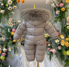 Light taupe padded baby snowsuit with large fur hood, displayed on a gold stand, surrounded by colorful flowers