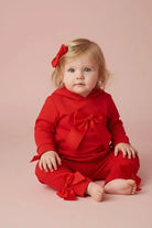 Toddler girl in red outfit with bows sitting on pink background