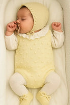 Sleeping baby in yellow knit bonnet and outfit with white tights and pacifier in soft crib