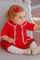 Toddler girl sitting on gray chair wearing red dress with plaid bows and white tights