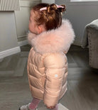 Toddler girl in pink puffer jacket with fur hood and pink hair clips indoors