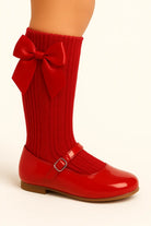 Child's leg wearing red knit socks with large bow and shiny red Mary Jane shoes