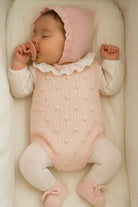 Sleeping baby in a pink knitted bonnet and bodysuit with white ruffled collar in a cozy crib