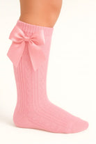 Close-up of a leg wearing pink cable knit socks with a large satin bow on the side