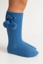 Close-up of legs wearing blue knit cable pattern socks with pom-pom bow detail