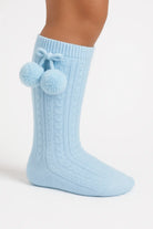 Light blue knitted knee-high sock with cable pattern and pom-pom tassels on the side
