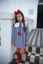 Young girl in blue striped dress with white collar and red bow, standing on black and white tiled steps
