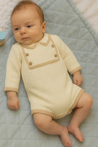 baby lying on quilted blue mat wearing cream romper with beige trim and wooden buttons