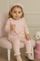 Toddler girl in pink ruffled outfit and headband sitting on pink chair with plush lamb toy