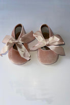 Pair of pink baby velvet pram shoes with large satin bows on a white background