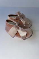 Pair of pink velvet baby pram shoes with large satin bows on plain background