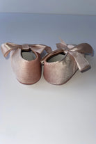 Pair of pink velvet baby pram shoes with satin bow ribbons on a white surface