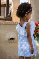 Young girl wearing pastel blue and pink plaid dress with white ruffle detail and matching headband outdoors