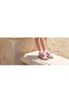 woman wearing pink glitter sandal with ankle ties standing on stone bench near sandy beach
