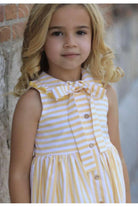 Young girl wearing sleeveless yellow and white striped summer dress with bow collar