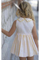 Child wearing yellow and white striped summer dress with ruffle collar walking outdoors