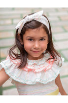 Smiling girl wearing white striped ruffled dress and matching bow headband in soft outdoor setting