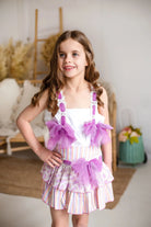 Girl wearing a colorful striped skirt with pink tulle bows and a white top, indoor setting