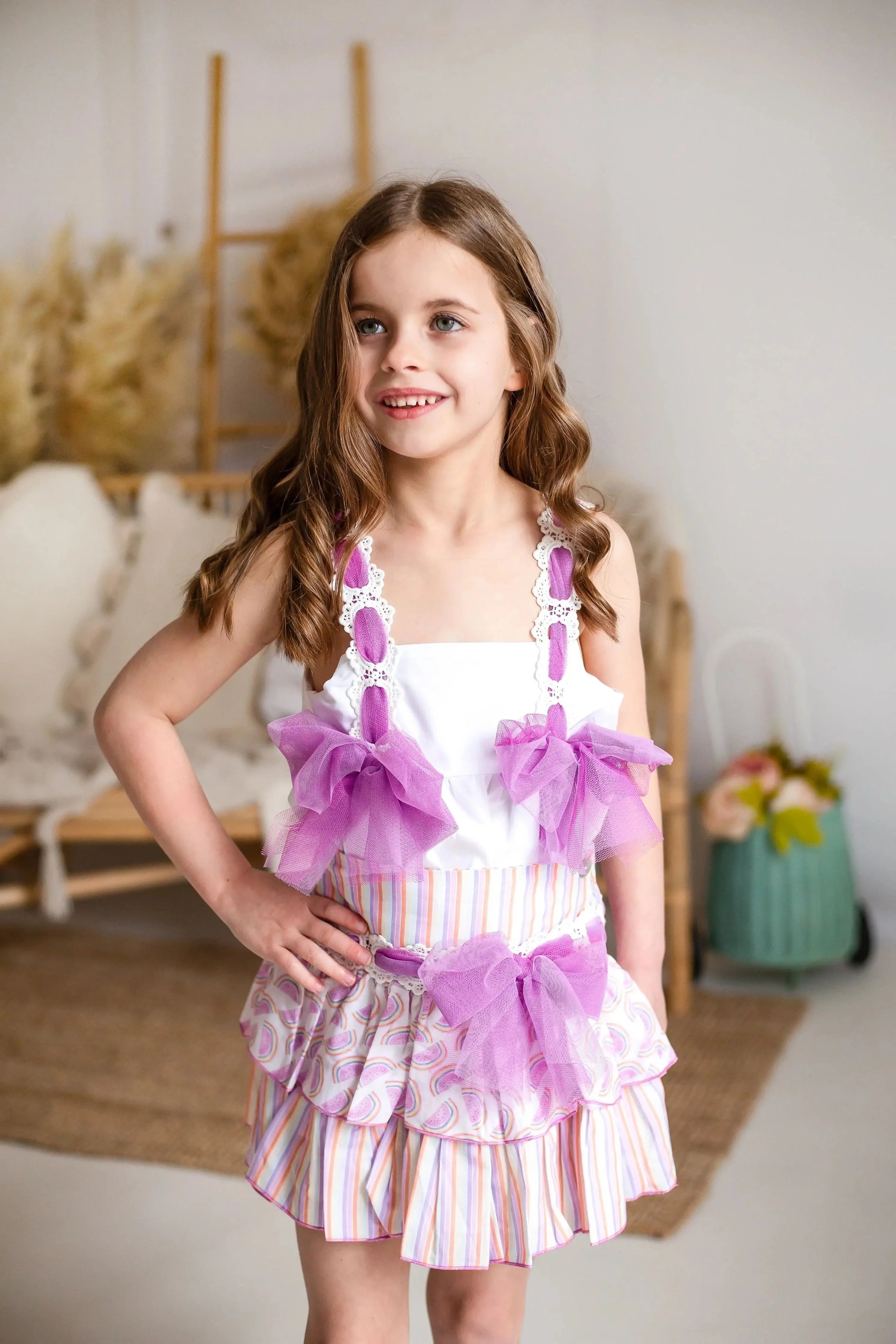 Girl wearing a colorful striped skirt with pink tulle bows and a white top, indoor setting