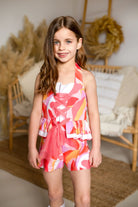 Smiling girl wearing colorful pink, red, and orange patterned summer outfit in cozy living room