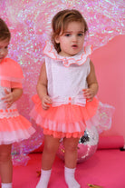Toddler girl in neon pink and white tulle romper with ruffled collar standing on pink floor with disco ball