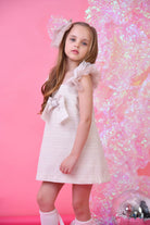 Young girl in glitter biscuit tulle dress with large bow and matching hair accessory on pink background